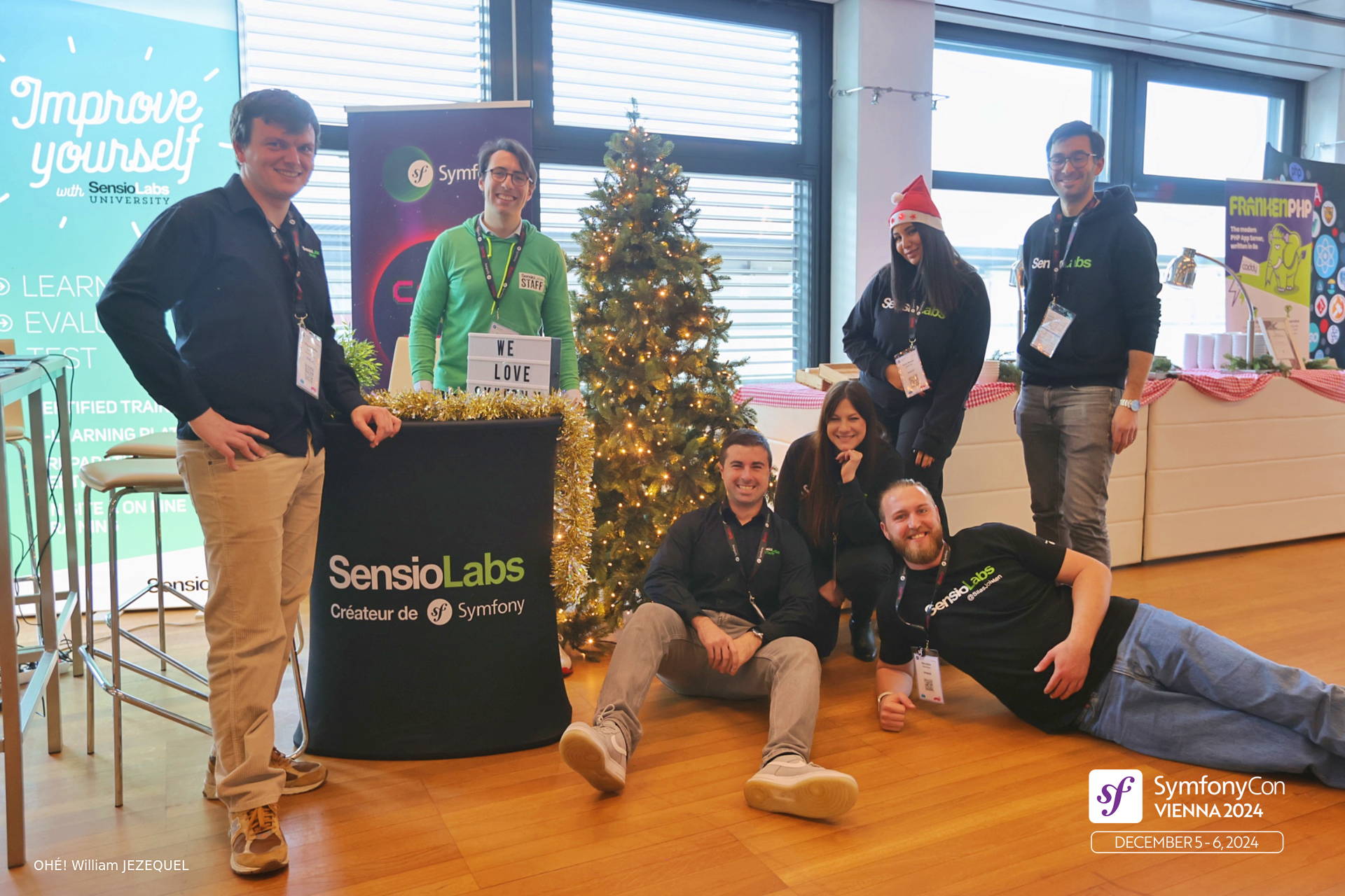 SensioLabs team members standing and sitting on the ground in front of the booth with a christmas tree at SymfonyCon Vienna 2024
