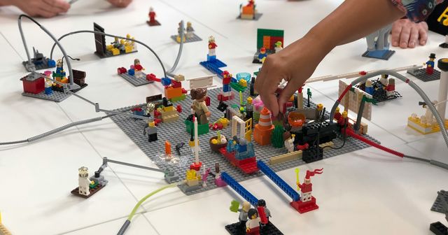 Many Lego figurines on a white table with hands playing with them