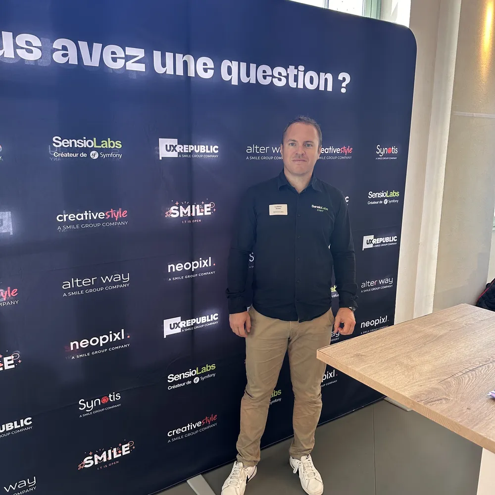 Ludovic Duval standing in front of a wall with SensioLabs logos and other brands of the Smile Group