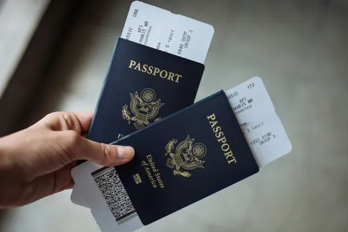 Two US passports with plane tickets inside with a hand holding them on the left