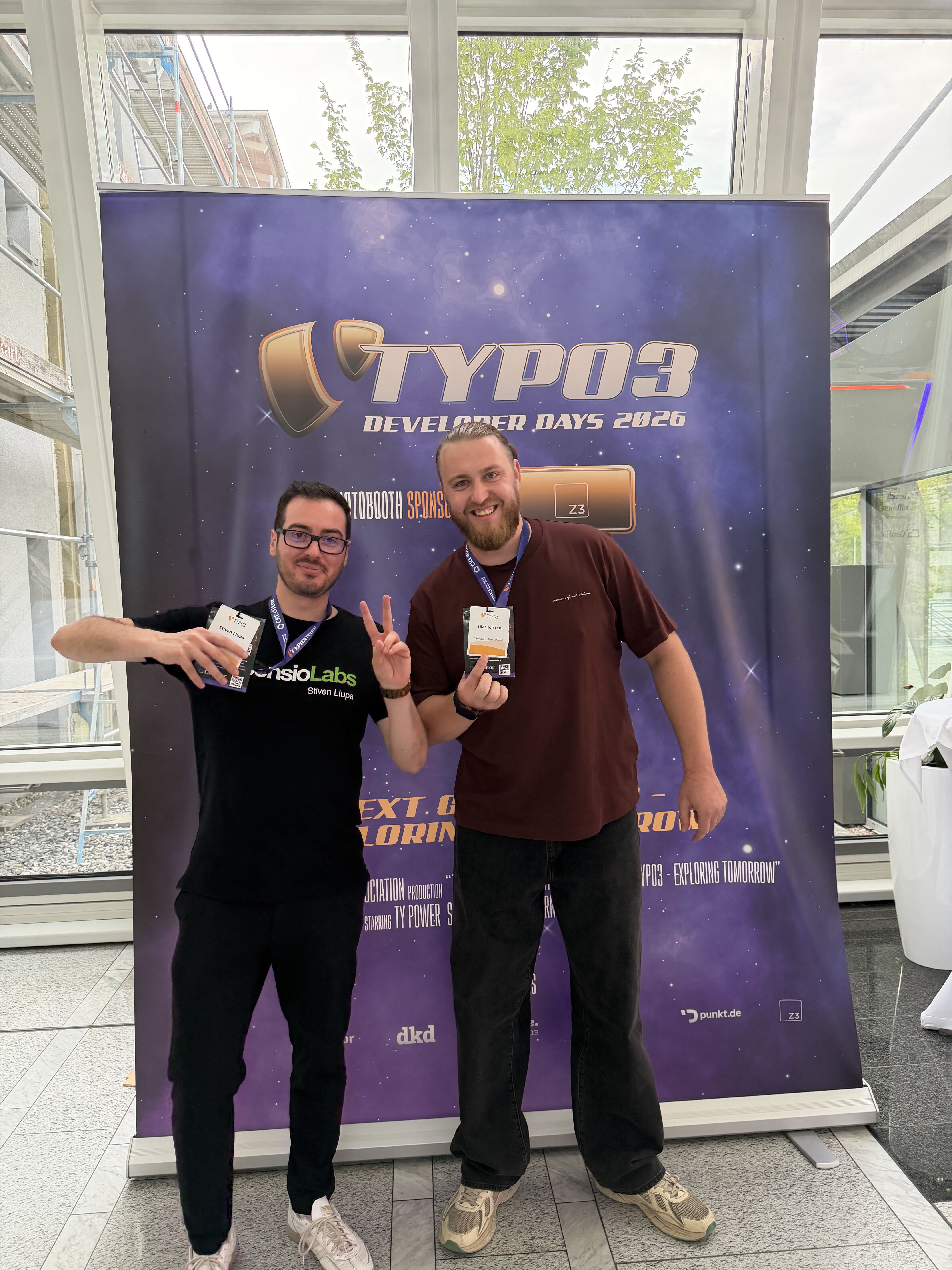 Two people smiling and posing with name tags in front of a TYPO3 Developer Days 2026 banner.