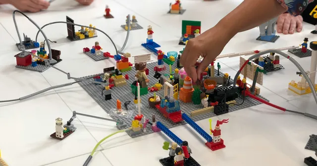 Many Lego figurines on a white table with hands playing with them