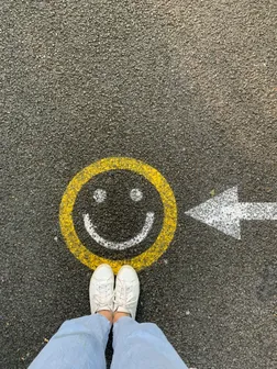 A yellow and white smiley on the ground with feets in sneakers