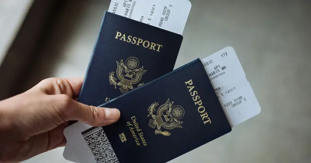 Two US passports with plane tickets inside with a hand holding them on the left