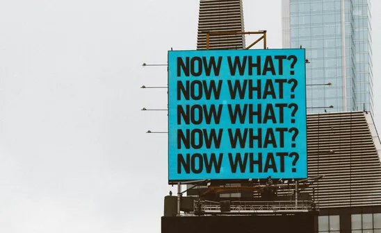 Blue sign on a building with several Now What? letters