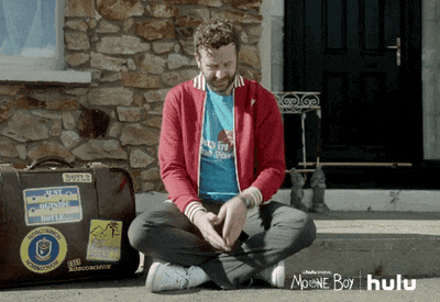 Moone Boy watching his watch sitting on the ground with a suitcase next to him