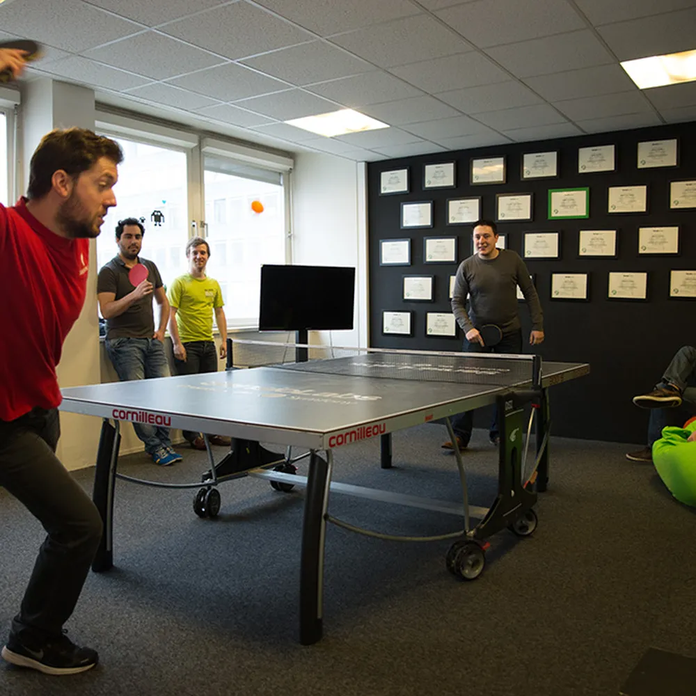 Young men playing ping pong in front of a wall full of diplomas